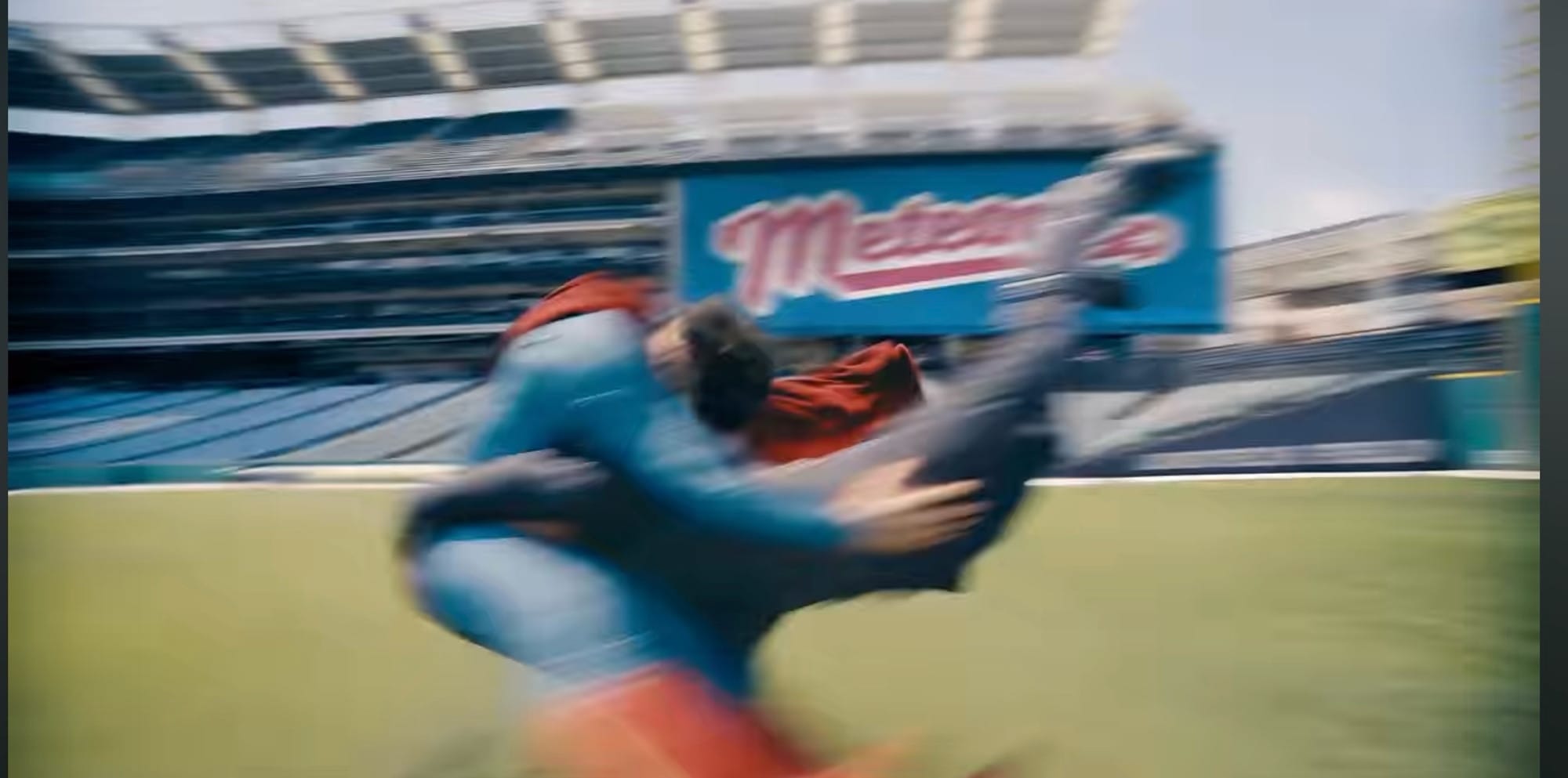 Superman collides with a villain on a baseball field. Behind him are stadium seats and the Metropolis Meteors logo.
